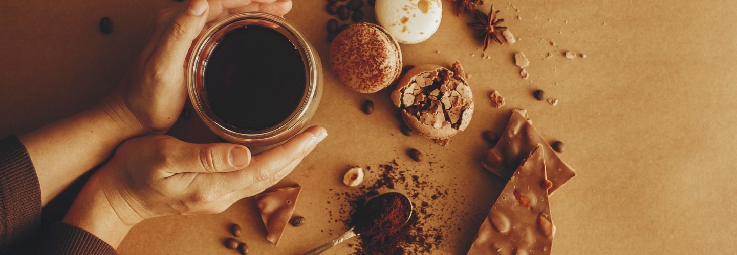 Hands holding glass cup with fresh coffee and roasted beans